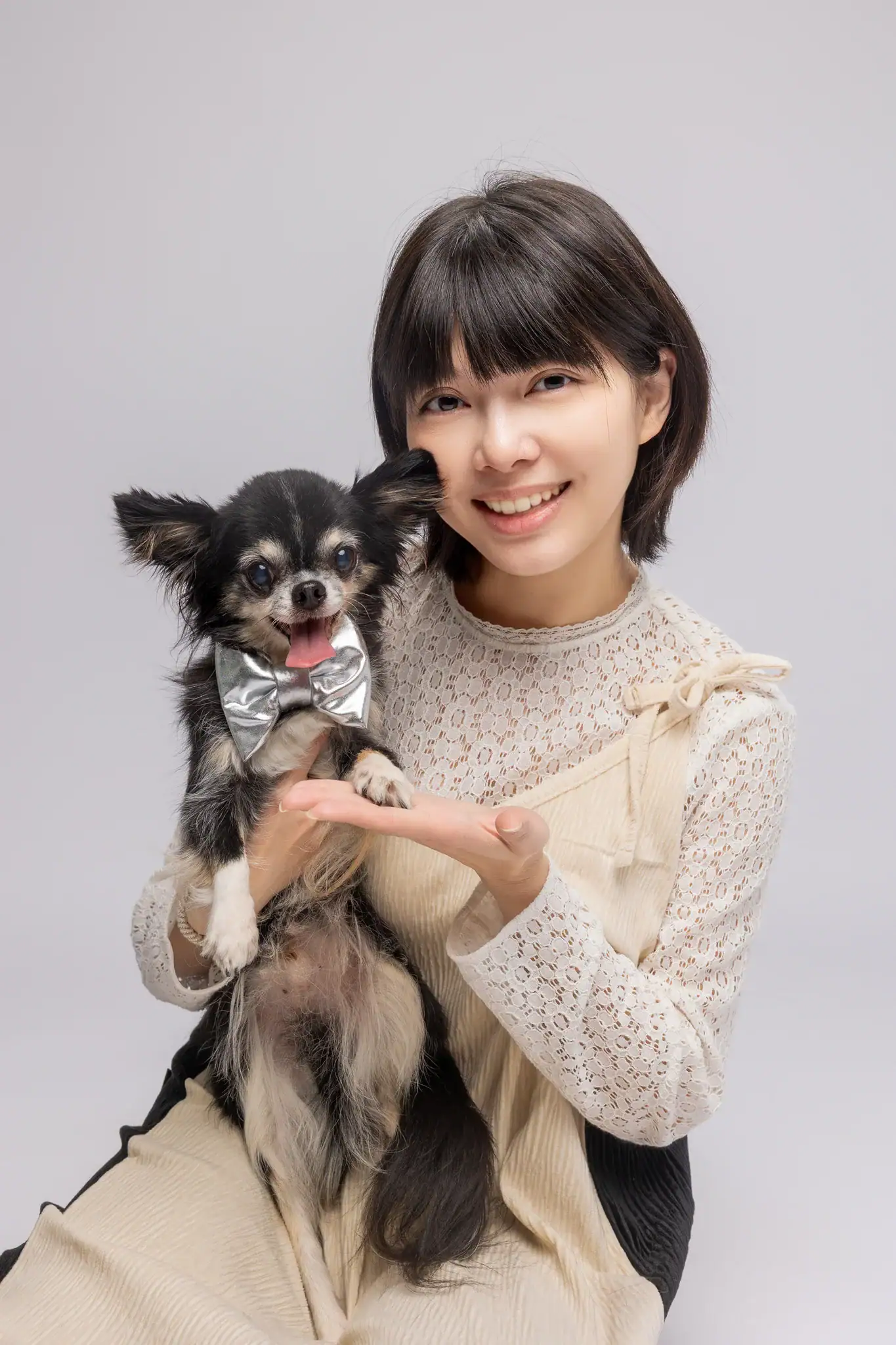 一位年輕女性（Lisa）懷抱著一隻戴銀色領結的黑棕長毛吉娃娃，兩人皆面帶笑容望向鏡頭，背景為淺灰色。