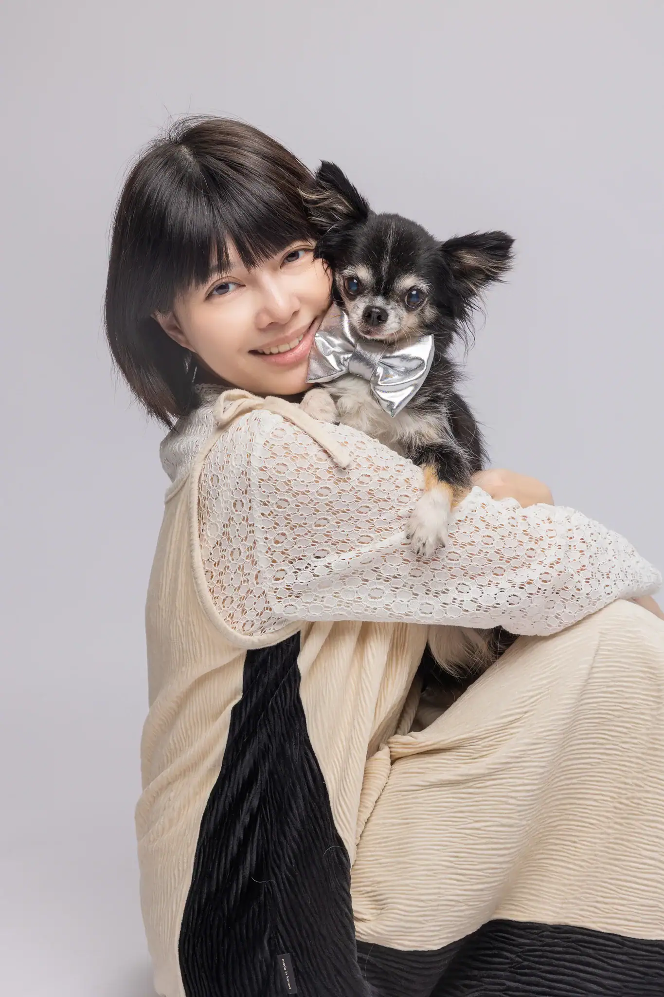 Lisa 側身緊緊擁抱著黑棕吉娃娃，狗兒依偎在她肩頭，兩人溫暖地看向鏡頭微笑。