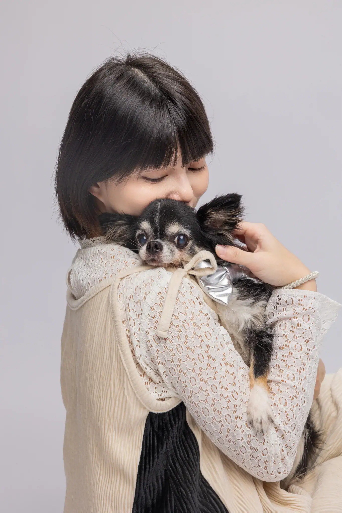 Lisa 閉眼輕輕擁抱黑棕吉娃娃，臉上洋溢著幸福的微笑，展現出寵愛與依戀。