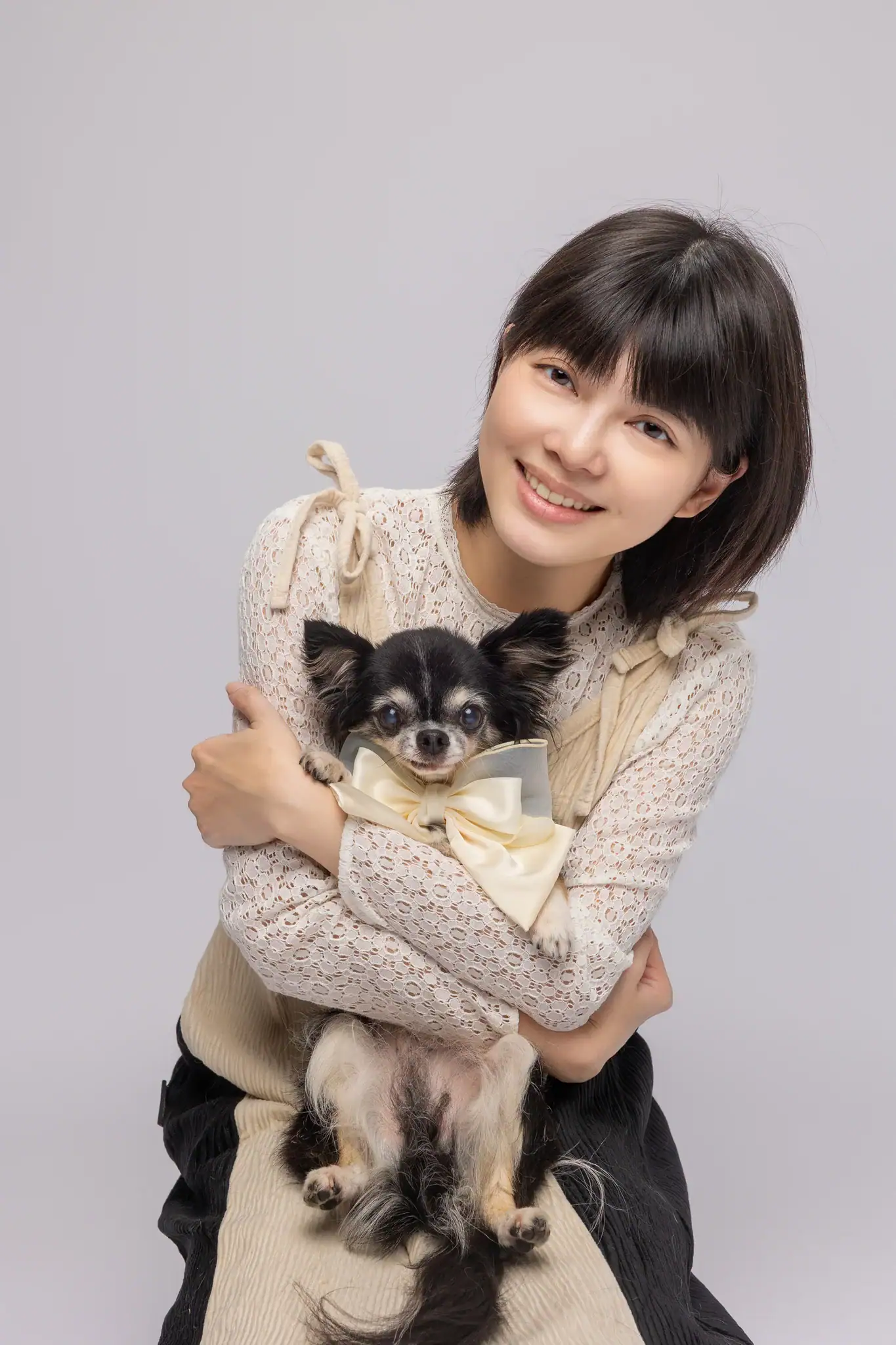 Lisa 懷抱著一隻戴著米色大領結的黑棕吉娃娃，兩人再次對著鏡頭露出燦爛笑容。