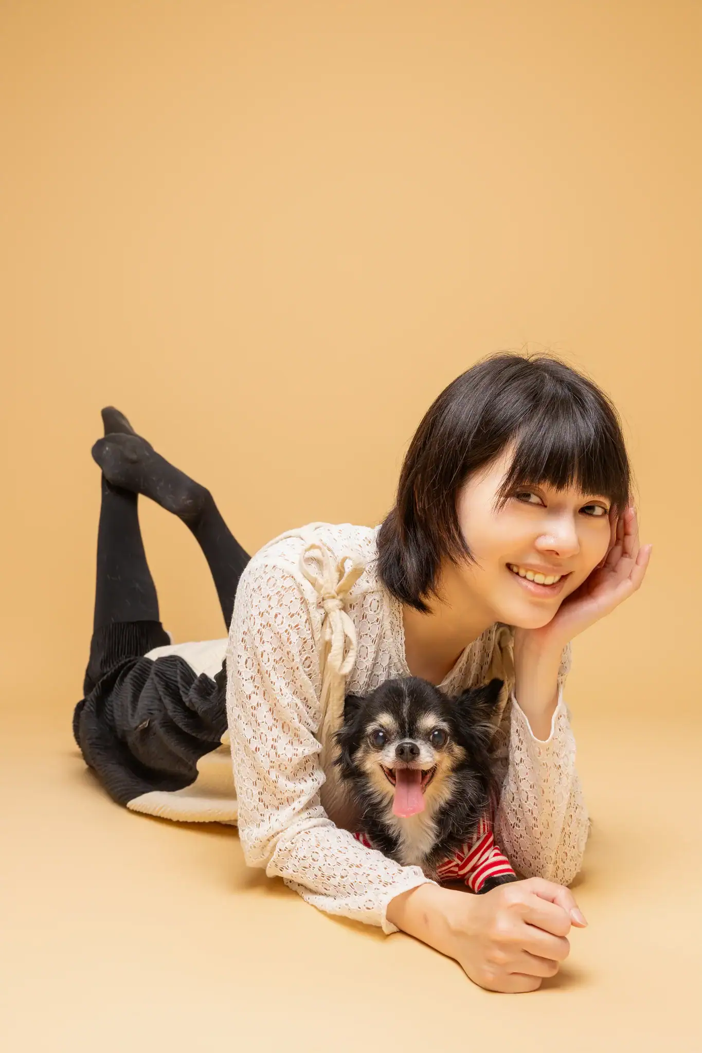 Lisa 趴臥，懷中抱著穿紅條紋衣的黑棕吉娃娃，一人一狗都露出可愛的笑容。