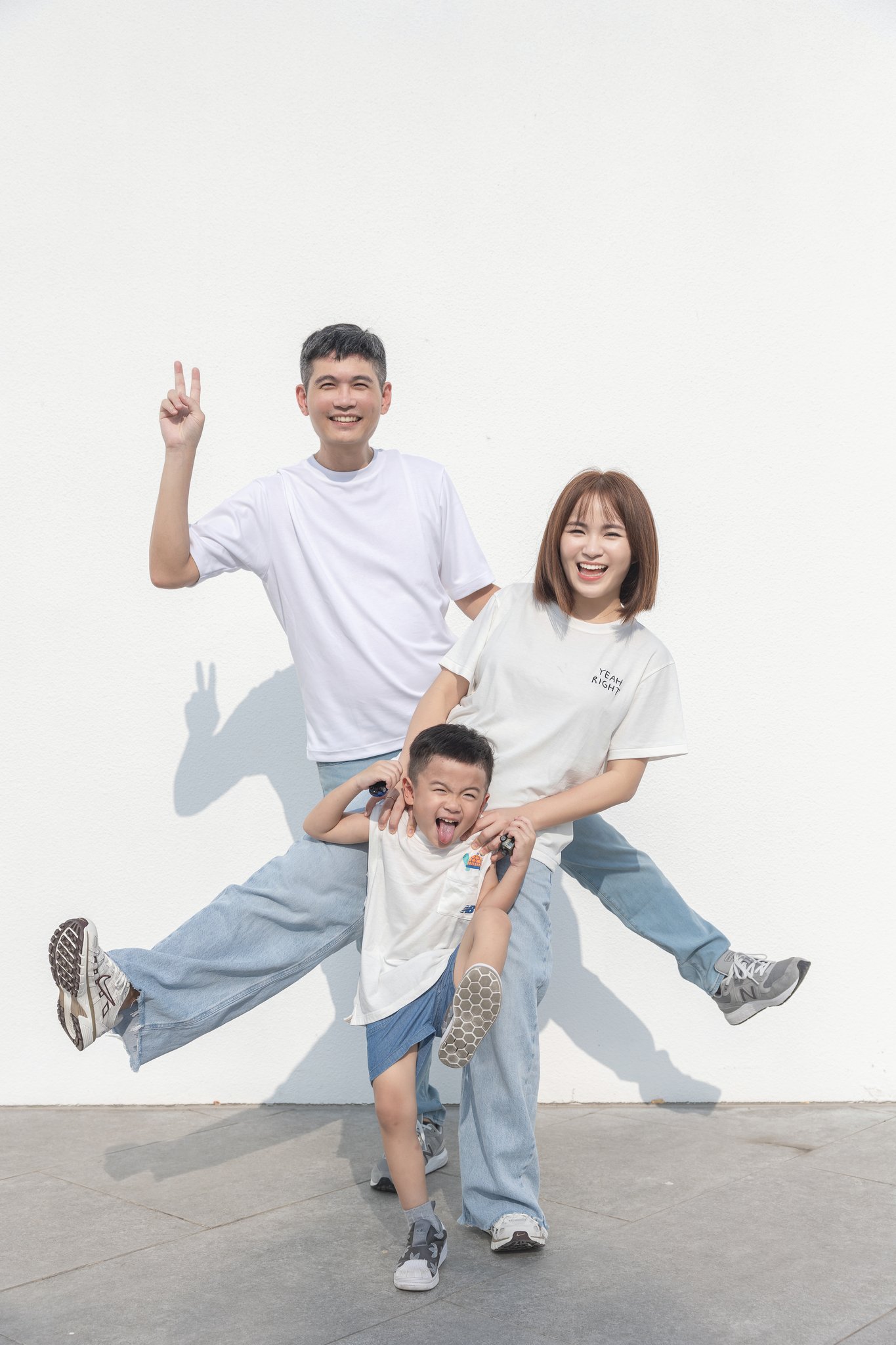 一家三口在白牆前跳躍，爸爸比YA、四歲品捷在中間扮鬼臉的親子寫真