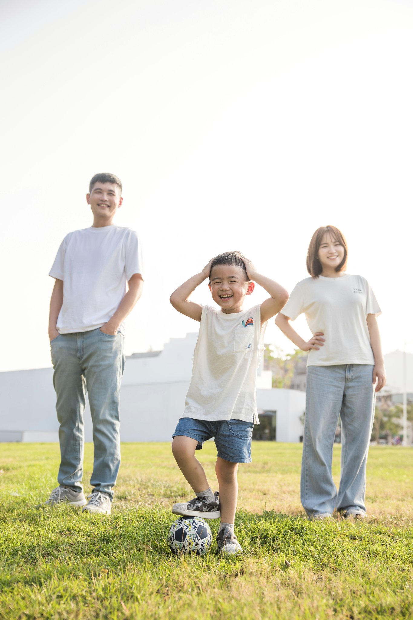 爸媽站在兩側、孩子帶著足球站在中間的草地全家福