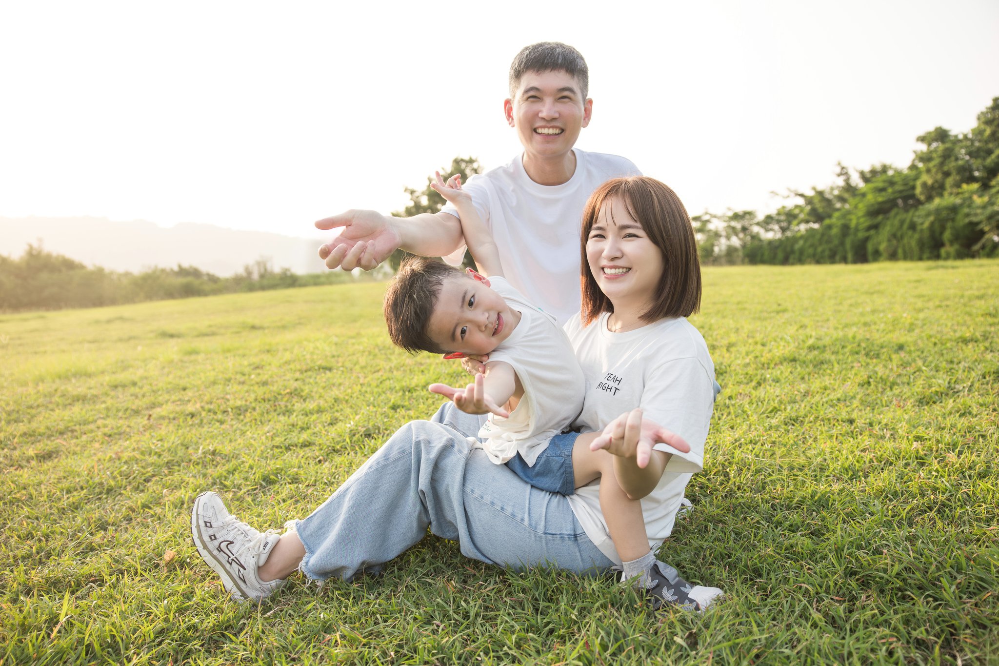爸媽坐在草地上，品捷橫躺在兩人腿上嬉鬧的全家福